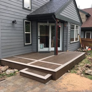 Two-toned wood porch to home with gray siding and diagonal glass front doors
