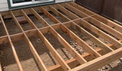 Framework for partially constructed wood deck behind house with white siding