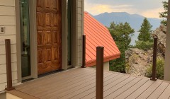 Composite wood front patio beside walnut front door to house with orange roof