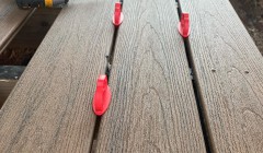 Close-up view of composite wood deck under construction with orange spacers, triangle and power drill