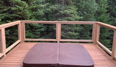 Covered hot tub built into wooden deck with cable railings overlooking forest