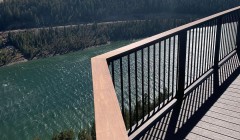 View of large lake and mountains from wooden deck with black metal railing