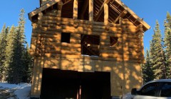 Partially constructed wood cabin on snowy day with adjacent silver SUV