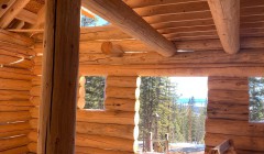 Interior view of partially-constructed log cabin overlooking forest and distant mountains