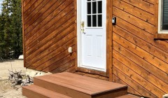 Cabin with diagonal wood siding and small wooden front patio with built-in step