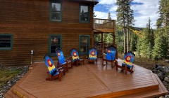 Large ground-level wooden deck with built-in step and six rocking chairs painted with Colorado state flag beside large cabin