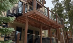 Wood decks with cable railings on all three levels of cream-colored home